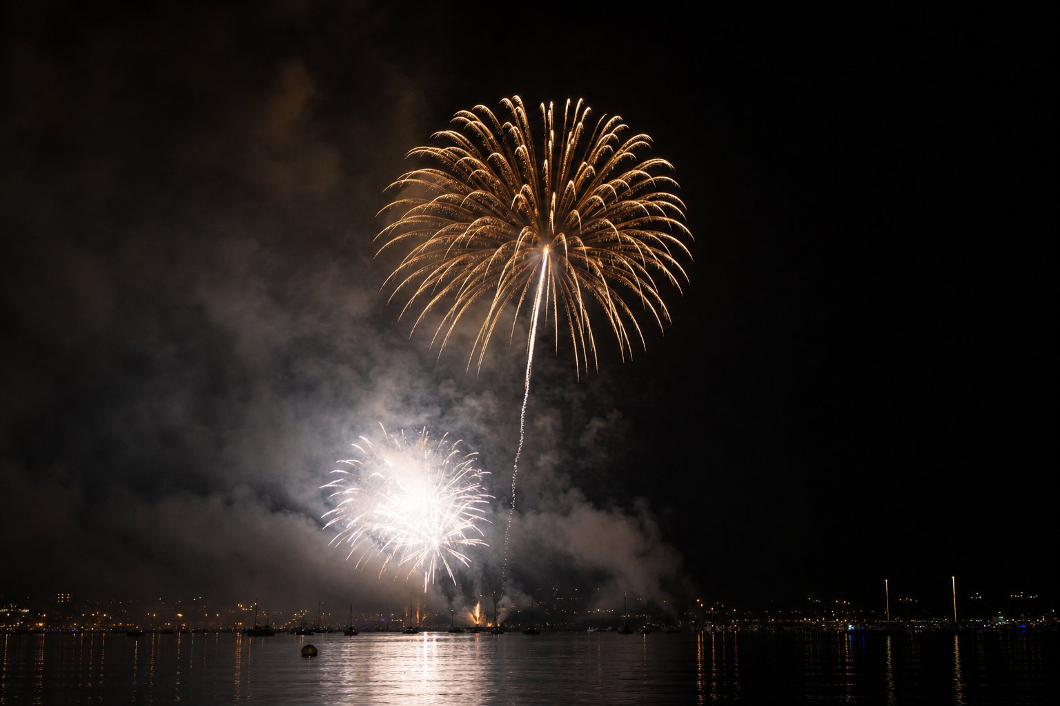 Black powder vs flash powder in fireworks — a golden aerial shell with a rising lift trail high over the water, and a bright white salute flash lower in the night sky